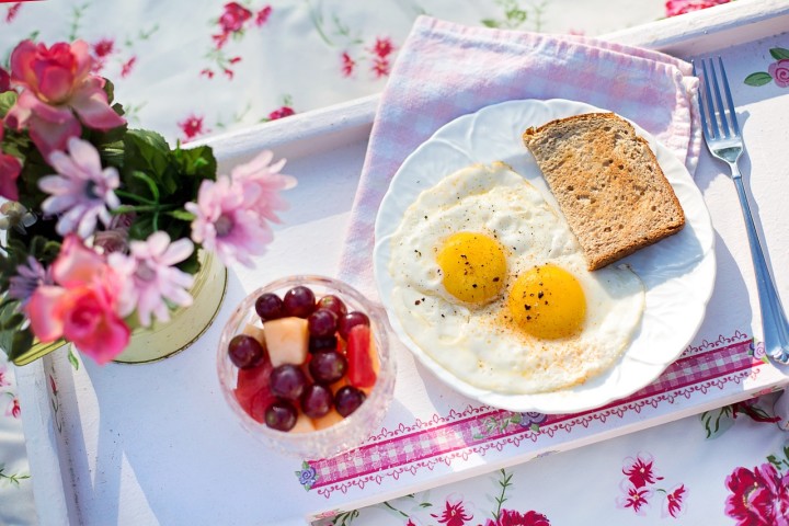 jajka sadzone na talerzyku przy kwiatach i chlebie