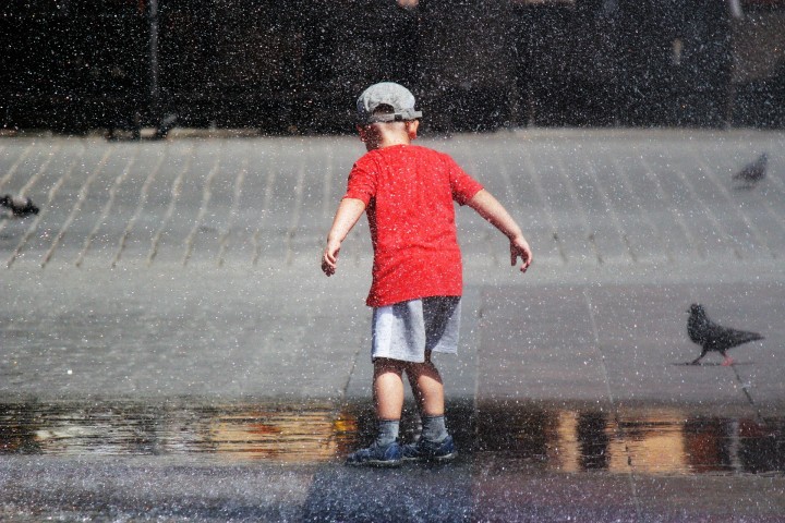 mały chłopiec biegający po placu w kroplach fontanny
